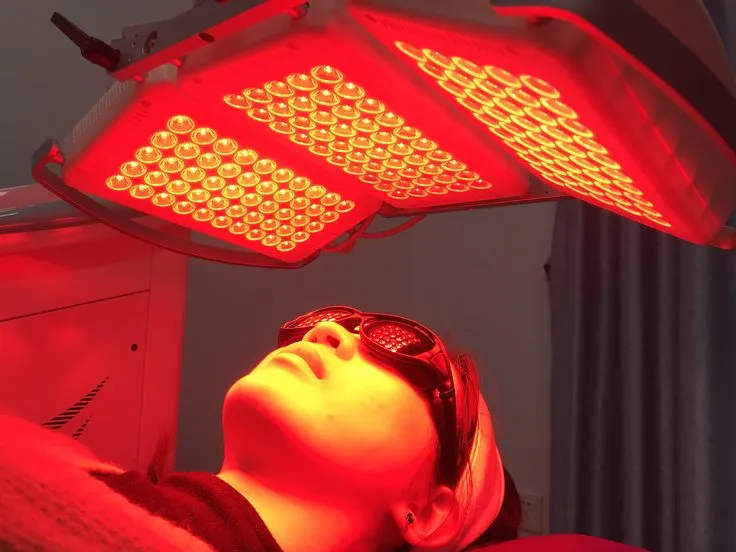 Person wearing protective goggles undergoing a red light therapy session with an LED device positioned above their face